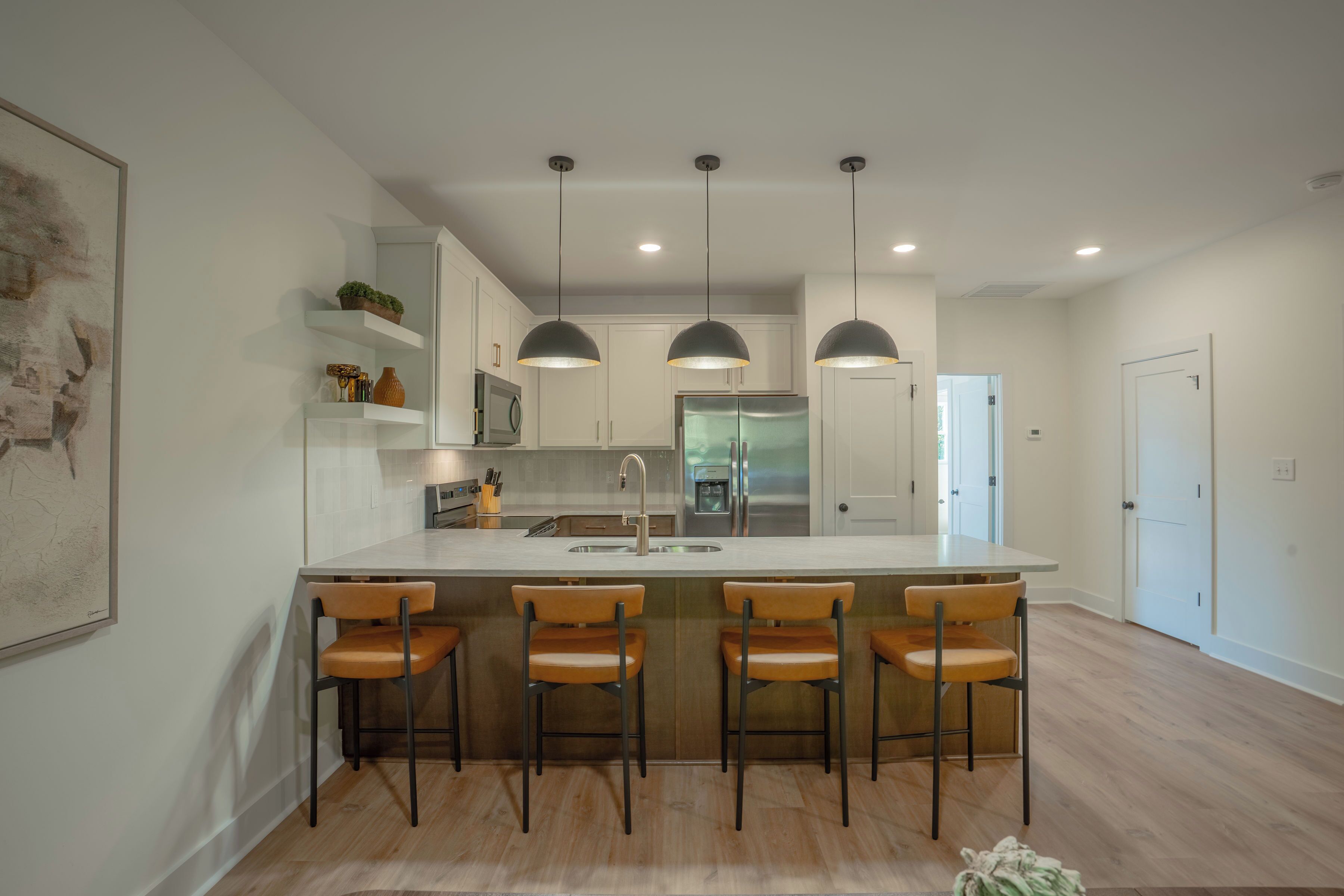 A modern kitchen with a central island, pendant lighting, and a view into the dining area.