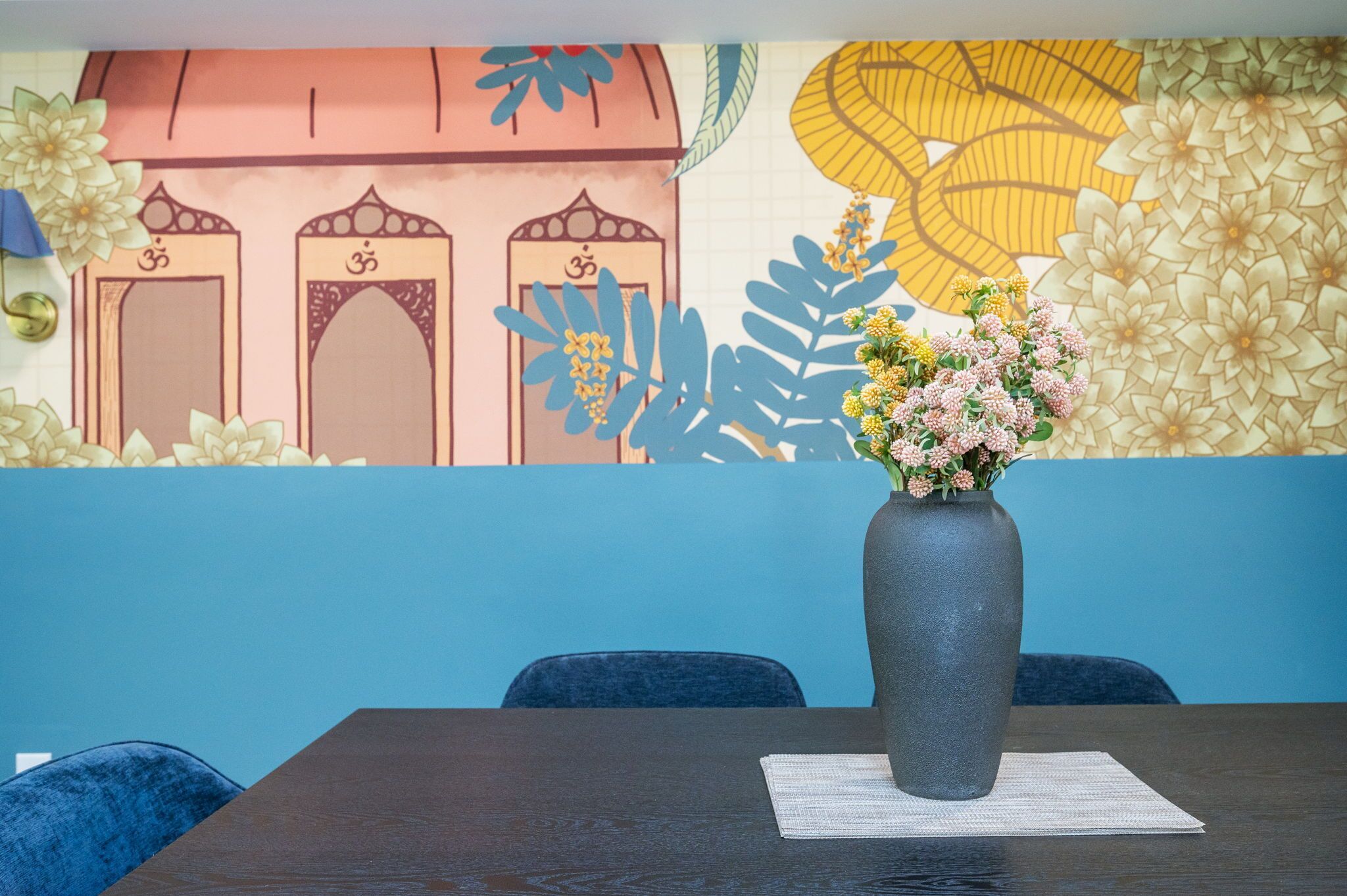 A room with a table, a vase with flowers, and a wall with a mural.