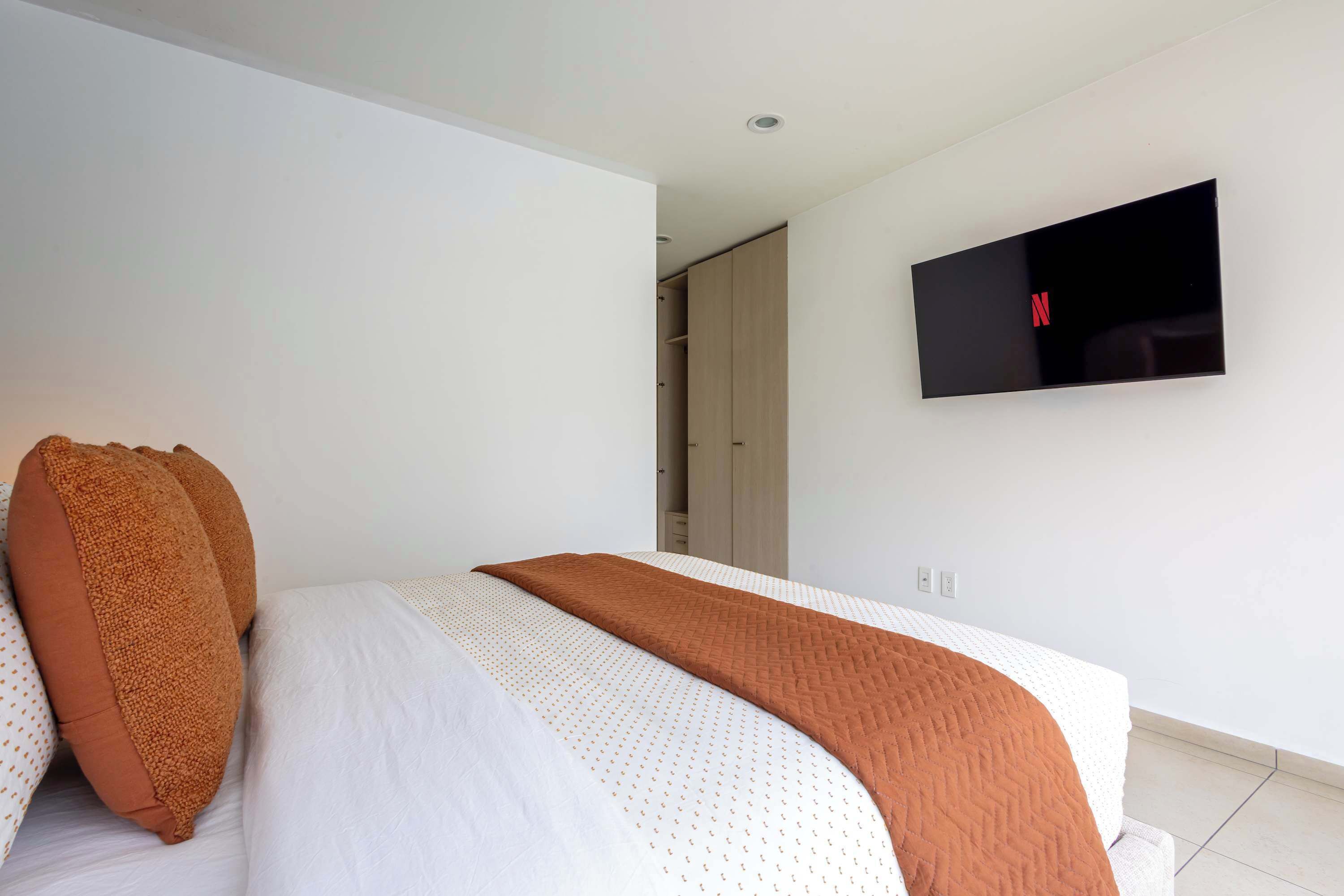 A bedroom with a bed, a TV mounted on the wall, and a door leading to another room.