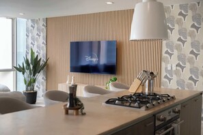 Une cuisine moderne dotée d’un téléviseur à écran plat fixé au mur, d’une cuisinière à gaz et d’un coin repas avec des chaises.