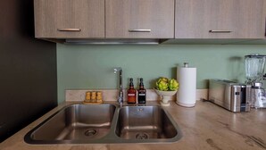 A kitchen with two stainless steel sinks, wooden cabinets, a green wall, a bowl of artichokes, a paper towel holder, a hand soap dispenser, a dish soap bottle, a hand soap bottle, a hand soap brush set, and a blender. - Casa Azul Sky Residence | Above Polanco |Sleeps 10 (Mexico City)