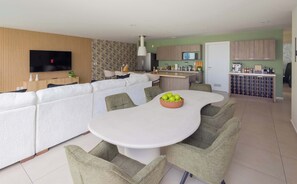 Ein modernes Wohnzimmer mit Sofa, Esstisch und Stühlen, einem an der Wand befestigten Fernseher sowie einer Küchenzeile mit Schränken und Geräten.