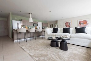 Ein modernes Wohnzimmer mit einem weißen Sofa, schwarzen und weißen Sesseln, einem Couchtisch und einer Küche im Hintergrund.