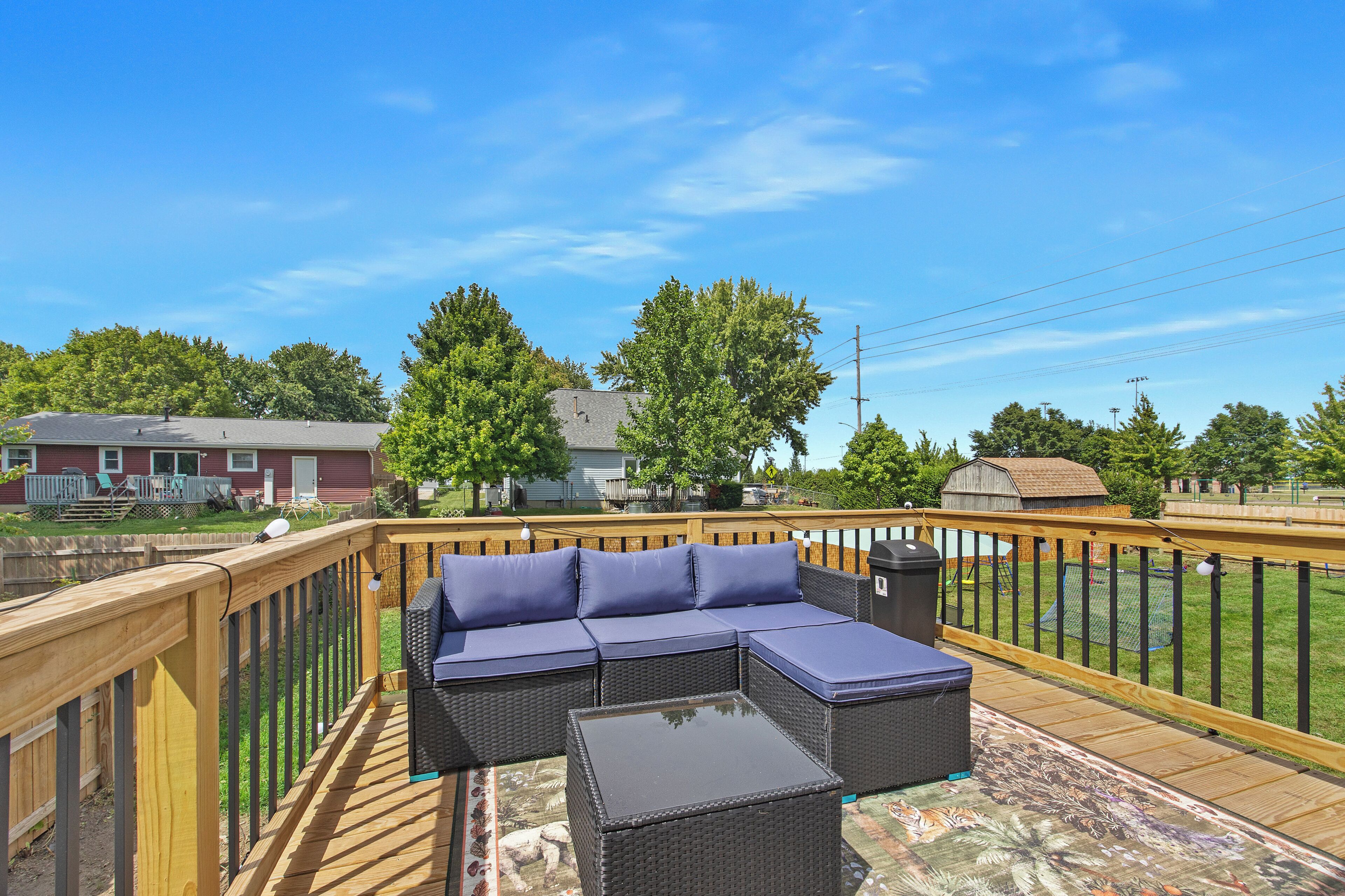 A deck with a sectional sofa and a coffee table, surrounded by a wooden railing.