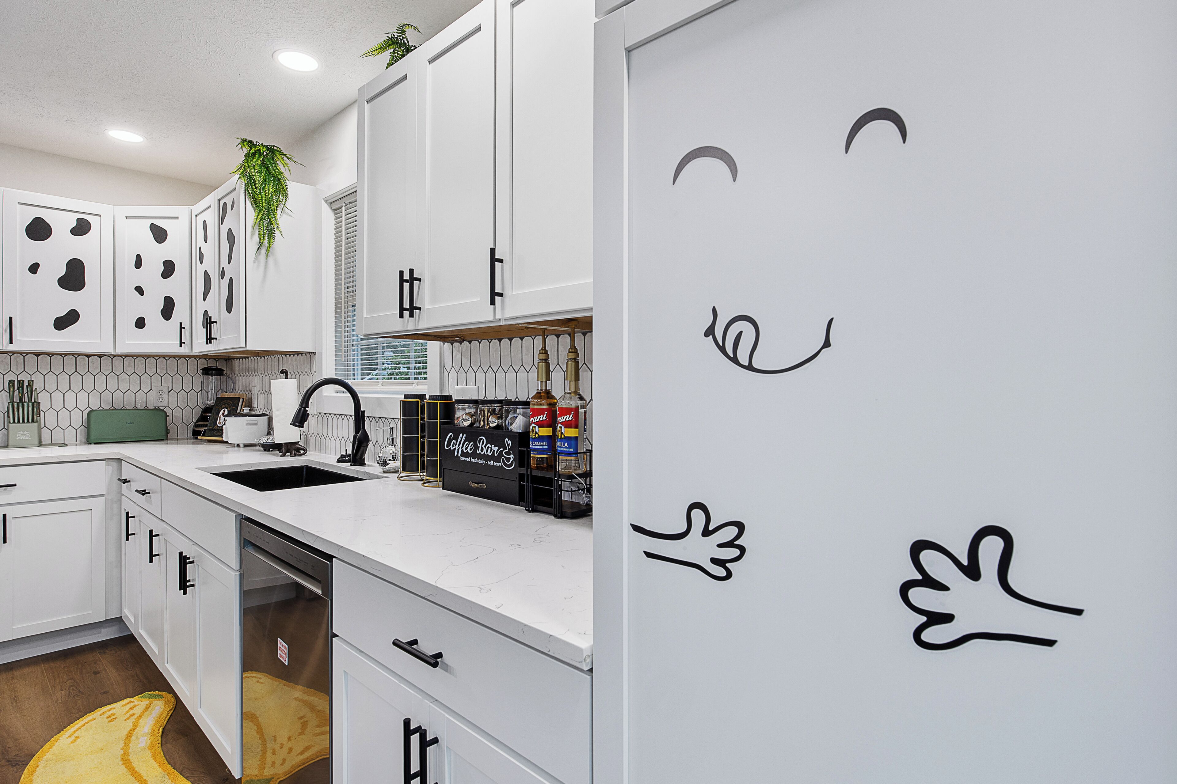 Een moderne keuken met witte kasten, een ingebouwde koffiehoek en een met de hand getekende smiley op de muur.