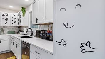Een moderne keuken met witte kasten, een ingebouwde koffiehoek en een met de hand getekende smiley op de muur.