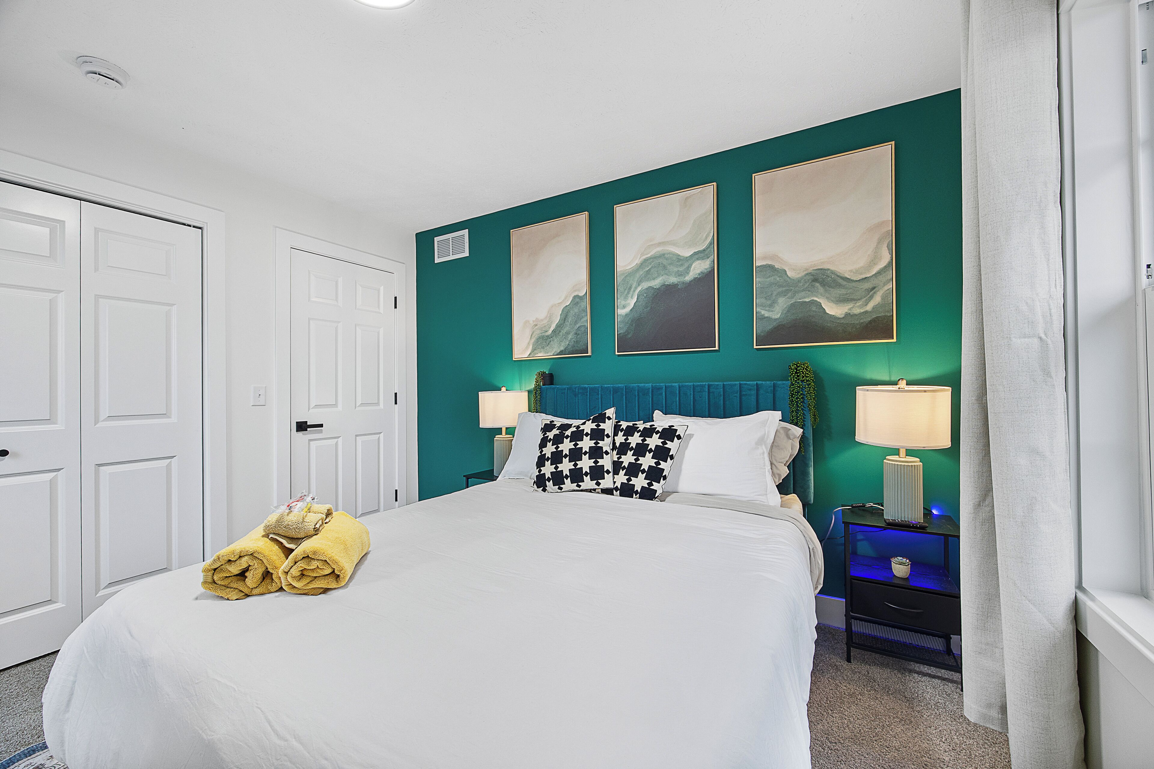 A hotel room with a bed, two bedside tables, a nightstand, a lamp, and artwork on the wall.