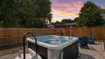 Ein Whirlpool in einem Garten mit Holzzaun, einem Stuhl und einem Kiesbereich.