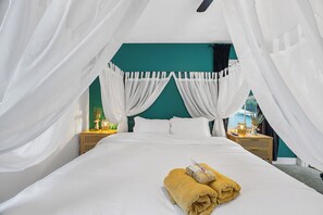 A bed with white linens, a canopy, and a pair of folded towels.