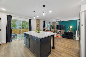 A modern kitchen with a central island, a dining area with a sofa and table, and a living room with a TV and seating.