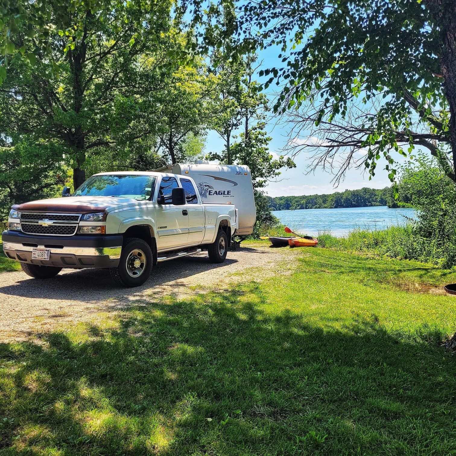 A Chevrolet truck parked beside a lake with a trailer labeled 'EAGLE' and kayaks on the shore.