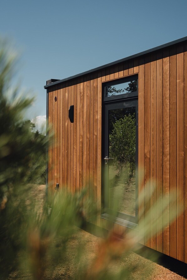 A modern wooden building with a large glass door and window, surrounded by greenery. - Experience Colorado’s golden hour from the comfort of your own luxury glass cabin. (Lake George)