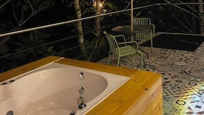 Een houten bad met betegelde vloer, omringd door groen en een tafel met stoelen.