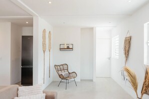 Una sala moderna con un sofá, una silla de mimbre y un refrigerador negro.