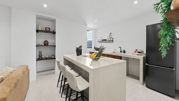 A modern kitchen with a central island, bar stools, a refrigerator, and a dining area with a sofa. - Kas Leon (Willemstad)