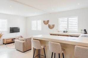 A modern kitchen with a central island, bar stools, a flat-screen TV, and decorative wall art.