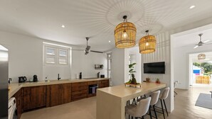 A modern kitchen with a central island, wooden cabinets, a built-in oven, and a ceiling fan. - Kas Leon (Willemstad)