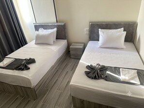 Habitación de hotel con dos camas, cada una con una almohada y una toalla doblada con cuidado.