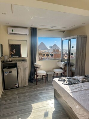Ein Hotelzimmer mit Bett, Schreibtisch, Kühlschrank, Spiegel und Blick auf eine Pyramide.