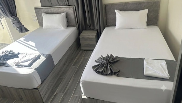 Ein Hotelzimmer mit zwei Betten, einem kleinen Tisch und einem Fenster mit Vorhängen.