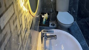 Ein Badezimmer mit einer Marmorplattenwand, einem weißen Waschbecken mit einem Wasserhahn, einer Toilette und einem Handtuchhalter mit gefalteten Handtüchern.