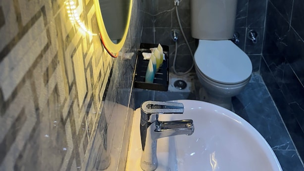 A bathroom with a marble-tiled wall, a white sink with a single faucet, a toilet, and a towel rack with folded towels. - Superb 4-bedroom hotel with AC in charming Giza Governorate (Al Haram)