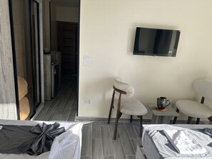 Una habitación de hotel con una cama, un televisor montado en la pared y una zona de estar con sillas y una mesa.