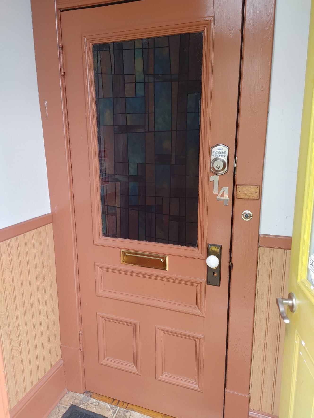 A brown door with a glass panel, a keypad lock, and a mailbox.