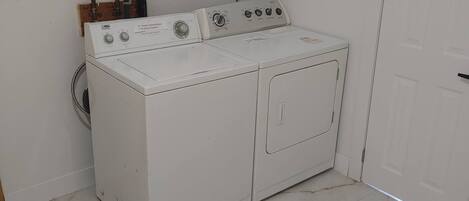 A laundry room with a white washer and dryer, a small shelf with a box, and a door.