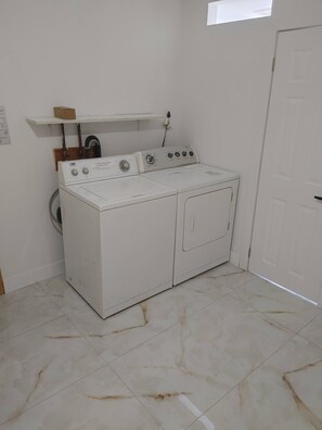 Un lavadero con lavadora y secadora blancas, un estante pequeño con una caja, y una puerta.