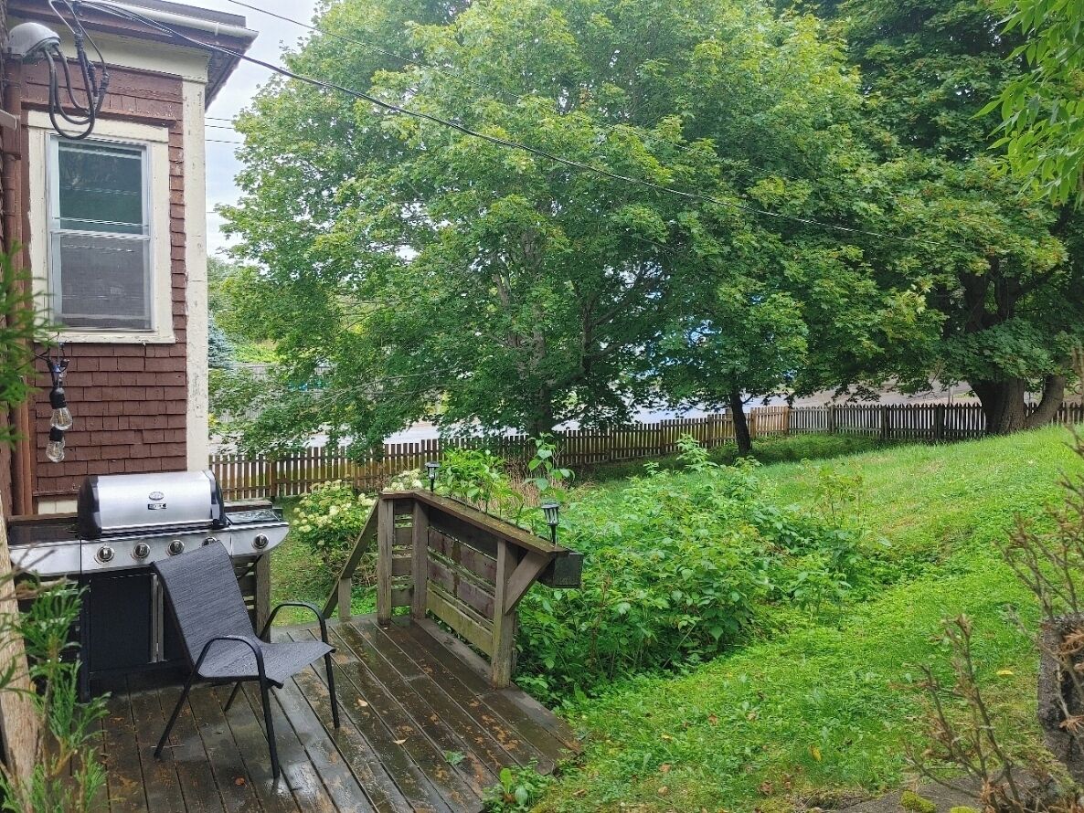 A backyard with a barbecue grill, a wooden deck, and a wooden fence.
