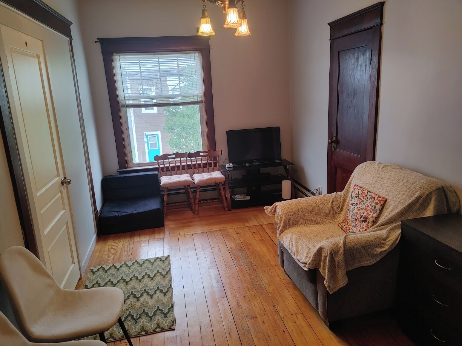 A living room with a sofa, a chair, a television, and a window with blinds.