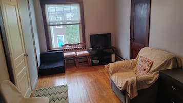 A living room with a sofa, a chair, a television, and a window with blinds.