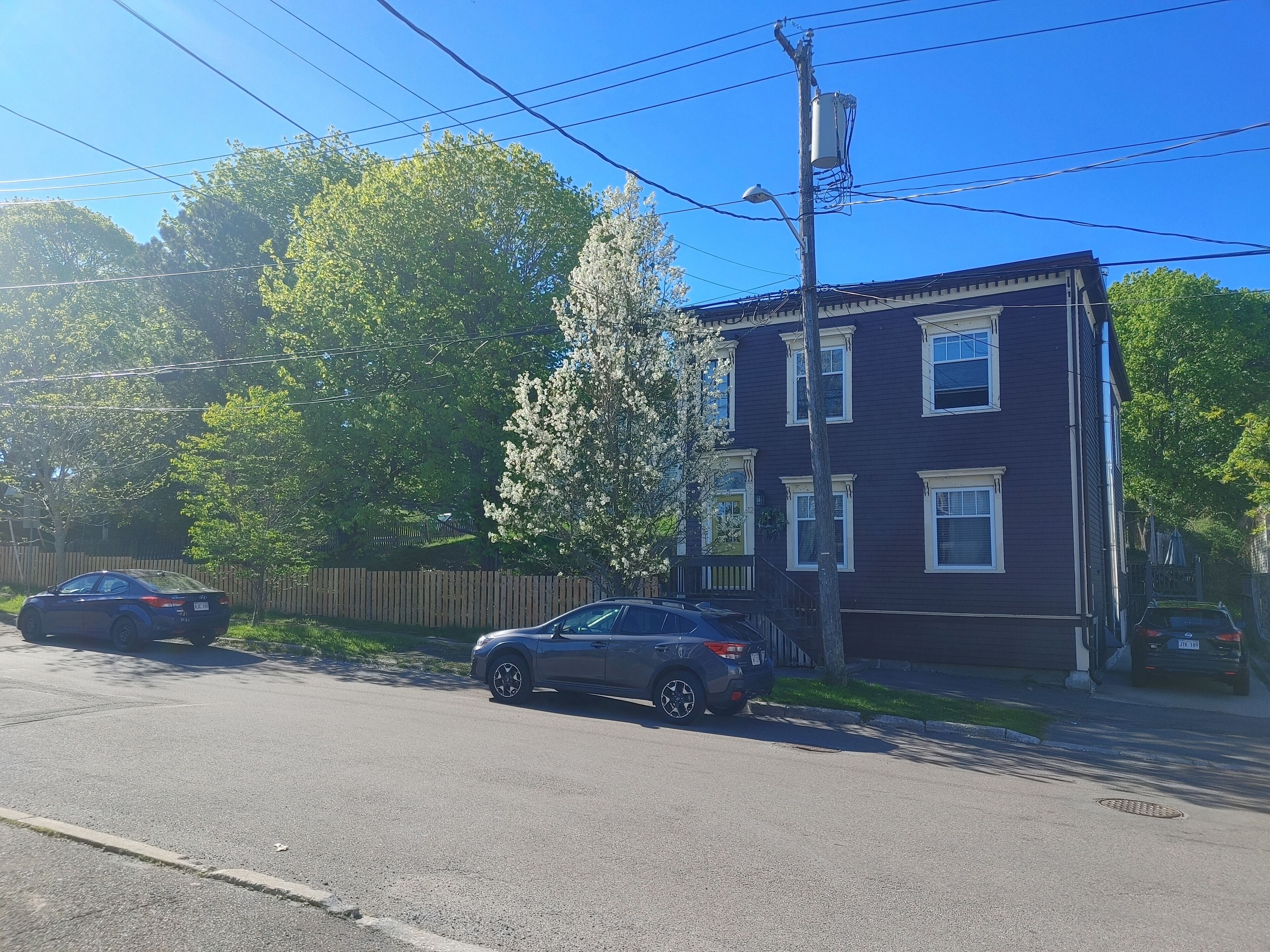 A residential street with a two-story house, parked cars, and a utility pole.