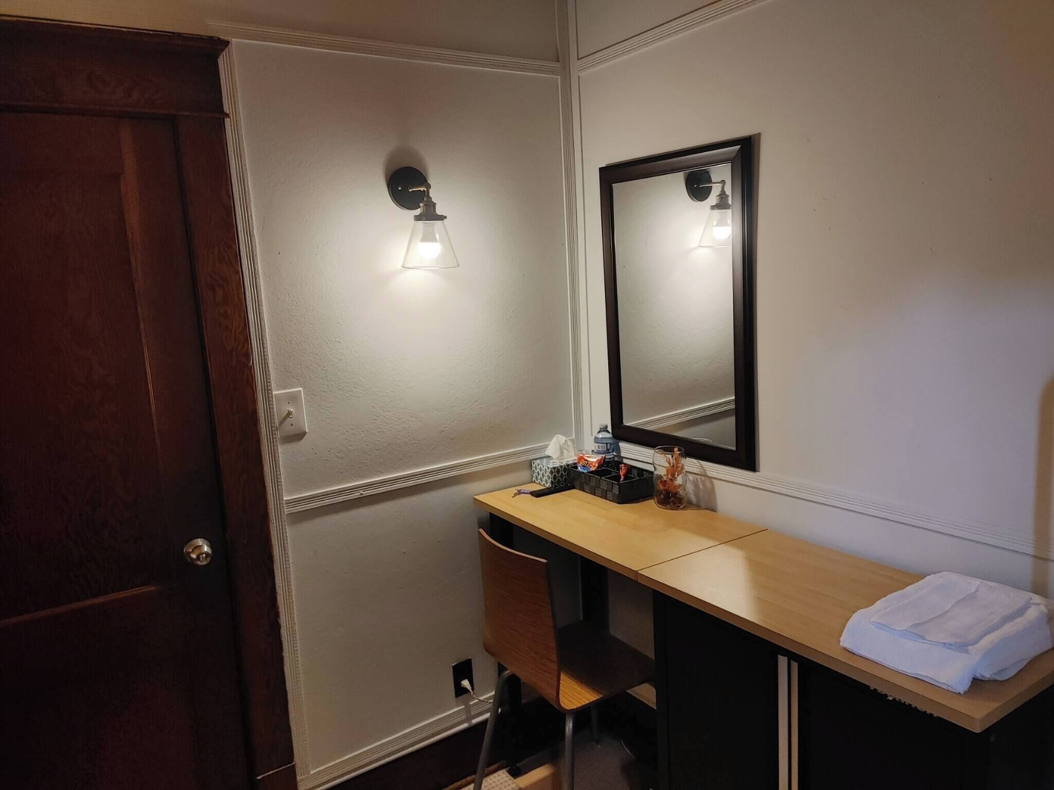 Un baño pequeño con tocador de madera, un espejo, una toalla y una lámpara en la pared.