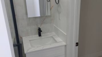 A bathroom with a white sink, mirror, and cabinets.