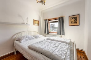 Een slaapkamer met twee eenpersoonsbedden, een raam met gordijnen, een radiator en een foto aan de muur.