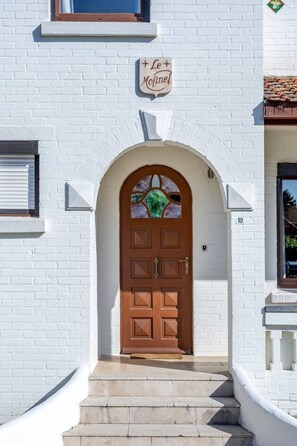 Un bâtiment blanc avec une porte marron, une enseigne au-dessus de la porte et une fenêtre sur la droite.
