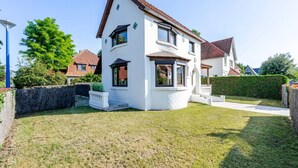 A two-story house with a white exterior, a brown roof, and a well-maintained lawn. - Le Molinel - vakantiewoning in hartje Koksijde (Koksijde)