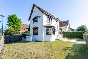 Ein zweistöckiges Haus mit weißer Fassade, braunem Dach und einem gepflegten Rasen.