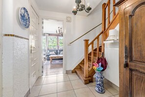 Ein Flur mit einer Holztreppe, einer Vase mit bunten Gegenständen und einem blau-weißen Teller an der Wand.