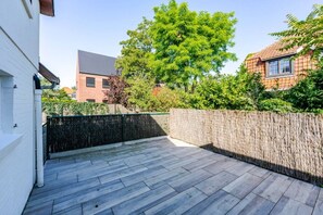 Eine Dachterrasse mit Holzdeck, weißer Wand und einer Hecke.