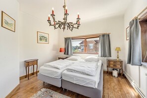 Ein Schlafzimmer mit Doppelbett, einer Kristallleuchter, einem Fenster mit Vorhängen, einem Nachttisch mit Lampe und einem gerahmten Bild an der Wand.