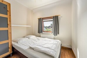 En säng för en person med en träram, ett fönster med gardiner och ett element.