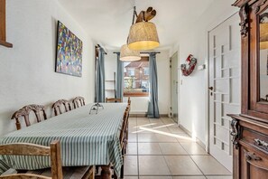 Ein Essbereich mit einem langen Tisch, Stühlen, einer hängenden Leuchte, einem Bild an der Wand und einer Tür mit einem dekorativen Spiegel.