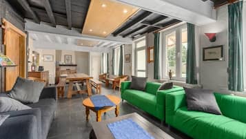 A spacious living area with a green sofa, a wooden coffee table, and a dining table with chairs.