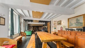 Una habitación amplia con una larga mesa de madera, bancos, sillas de mimbre y un sofá verde, además de una chimenea.