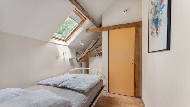 Un dormitorio con tragaluz, una cama, una puerta de madera y un cuadro enmarcado en la pared.