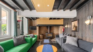 Una sala de estar moderna con chimenea, sofás verde y gris, una mesa redonda de madera y un ventanal grande.