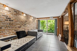 A room with a brick wall, a sofa, a bed, and a view through a glass door.